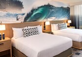A hotel room with two beds, a large wave mural on the wall, and a view of the beach.