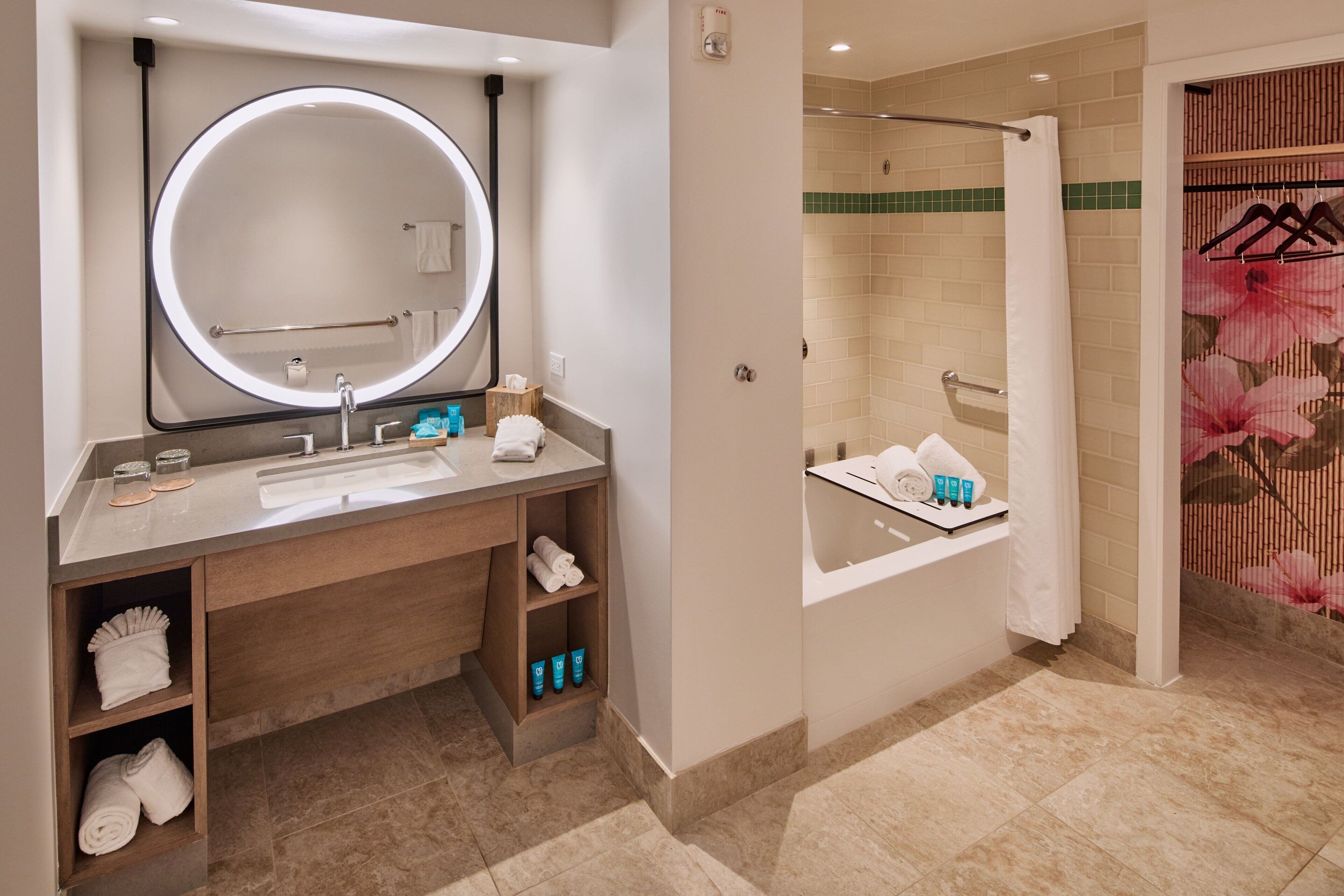 A modern bathroom with a round mirror, a sink, a shower, and a glass-enclosed bathtub.