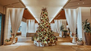 A spacious lobby with a large Christmas tree decorated with ornaments and lights, surrounded by potted plants and a seating area.