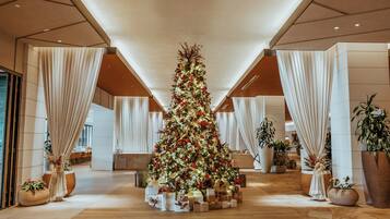 Un vestíbulo amplio con un gran árbol de Navidad decorado con adornos e iluminación, rodeado de plantas en macetas y una zona de estar.