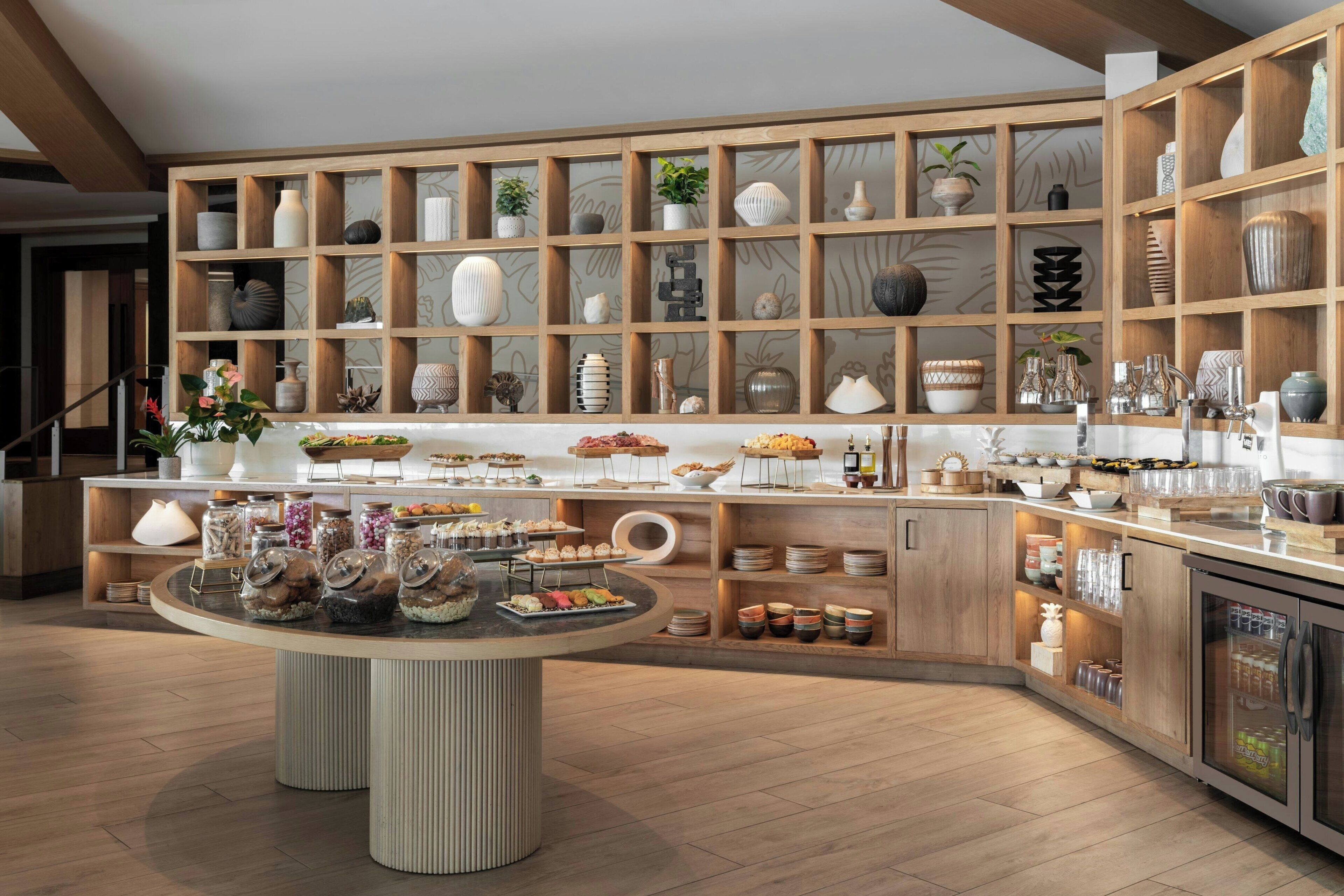 Une cuisine moderne avec des meubles en bois, un îlot central où sont exposés des aliments, ainsi qu’une variété d’ustensiles de cuisine et d’objets décoratifs disposés sur des étagères.