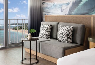 A modern hotel room with a balcony, a large ocean view, a sofa with patterned cushions, and a small side table with a vase.