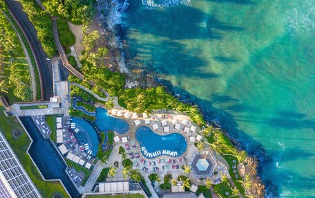 An aerial view of a resort with multiple swimming pools, a beach area, and lush greenery.
