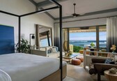 A modern hotel room with a large bed, a balcony with ocean views, and a seating area with a table and chairs.
