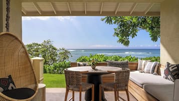 A patio with a round table, two chairs, a sofa, and a hanging chair. The patio overlooks a view of the ocean.