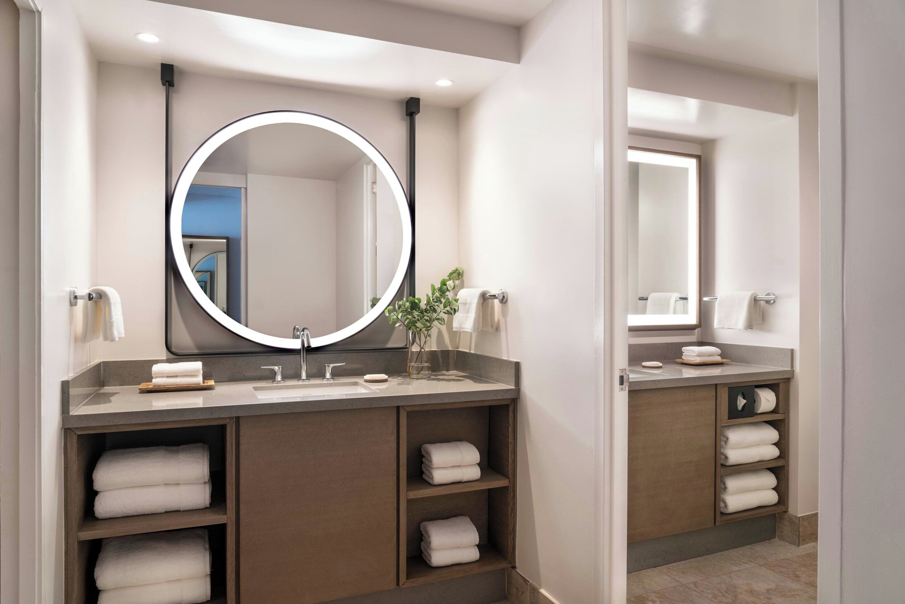 A modern bathroom with a round mirror, built-in shelves for towels, and a vanity with a sink.
