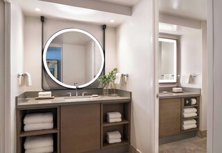A modern bathroom with a round mirror, built-in shelves for towels, and a vanity with a sink.