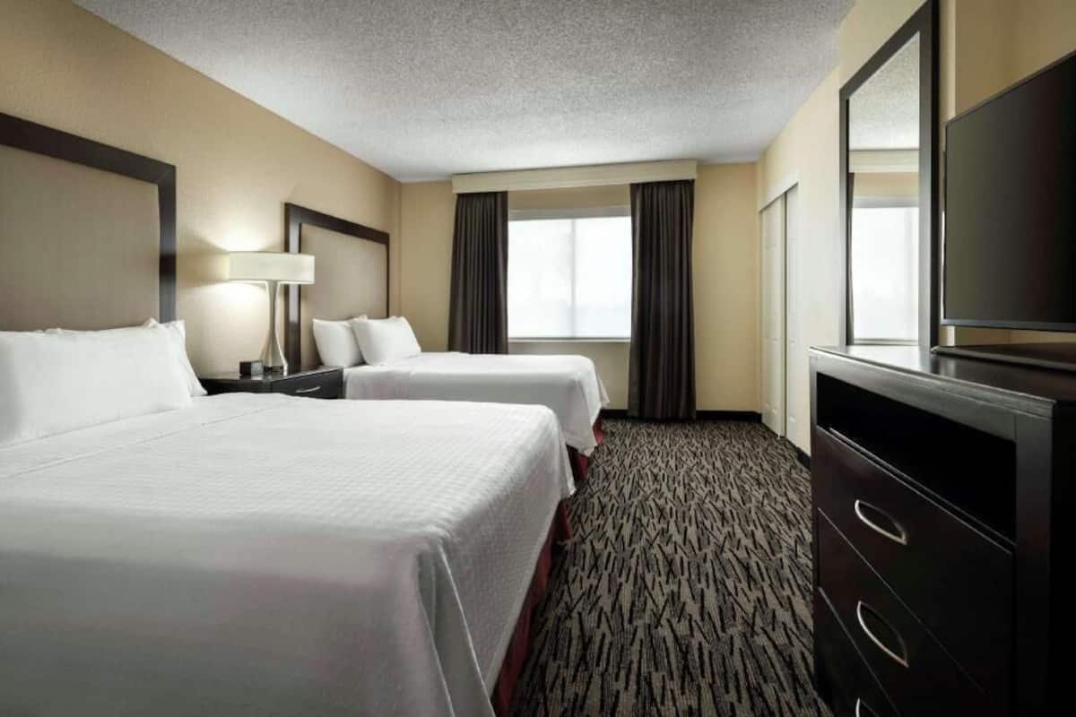 A hotel room with two beds, a TV, a desk, and a large window.