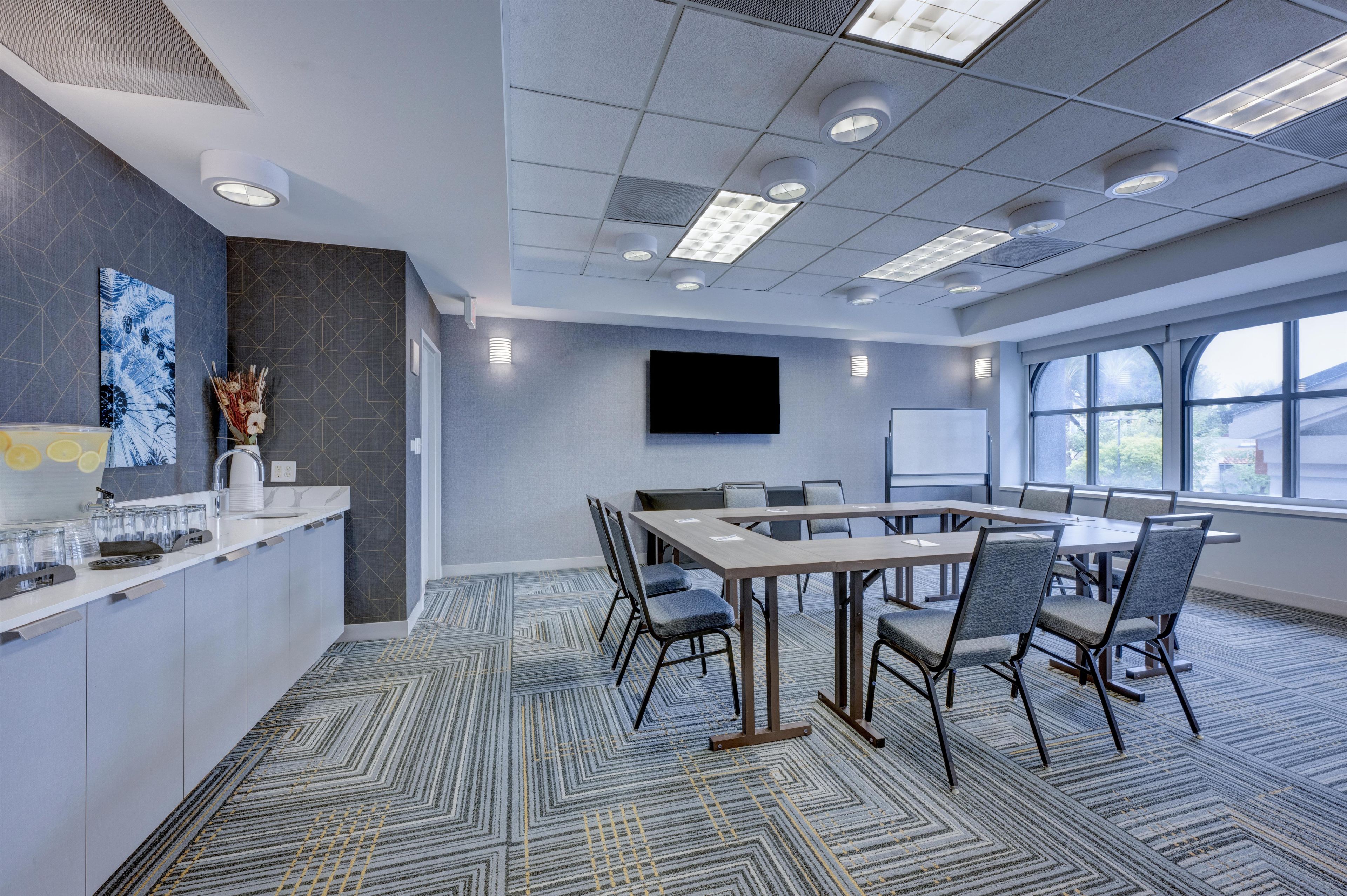 A conference room with a long table, chairs, a flat-screen TV, and a large window.