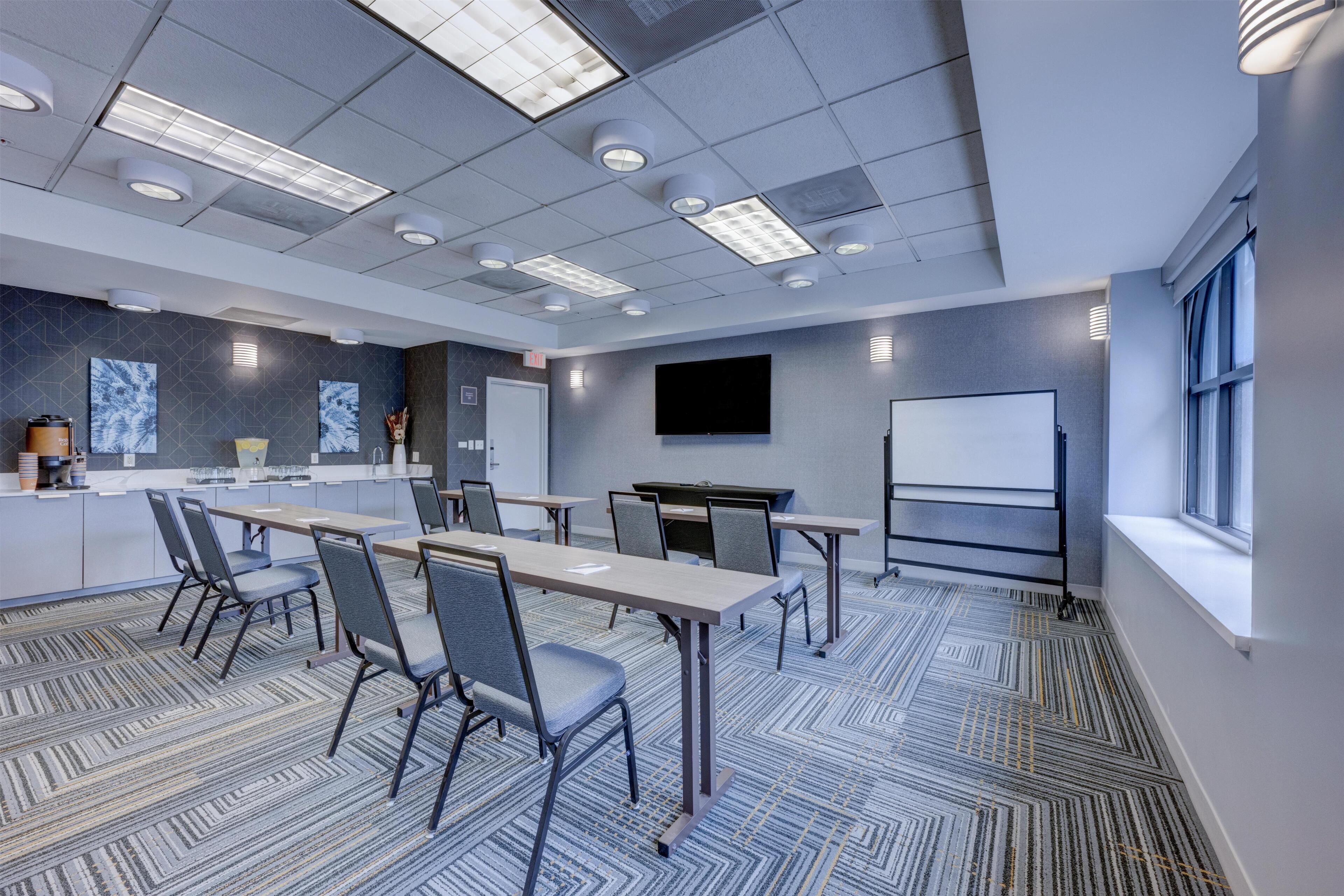 A conference room with a long table, chairs, a whiteboard, and a projector screen.