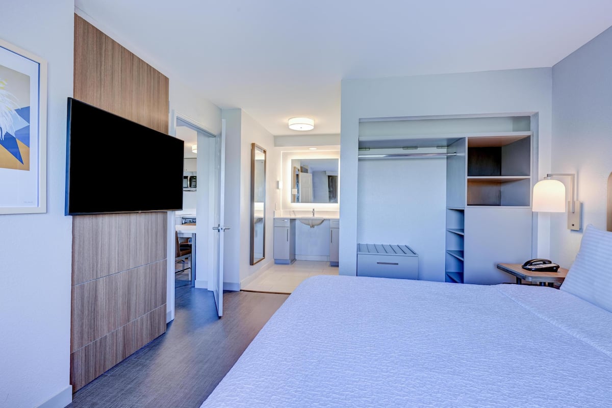 A hotel room with a bed, a wardrobe, a TV, a desk, and a bathroom.