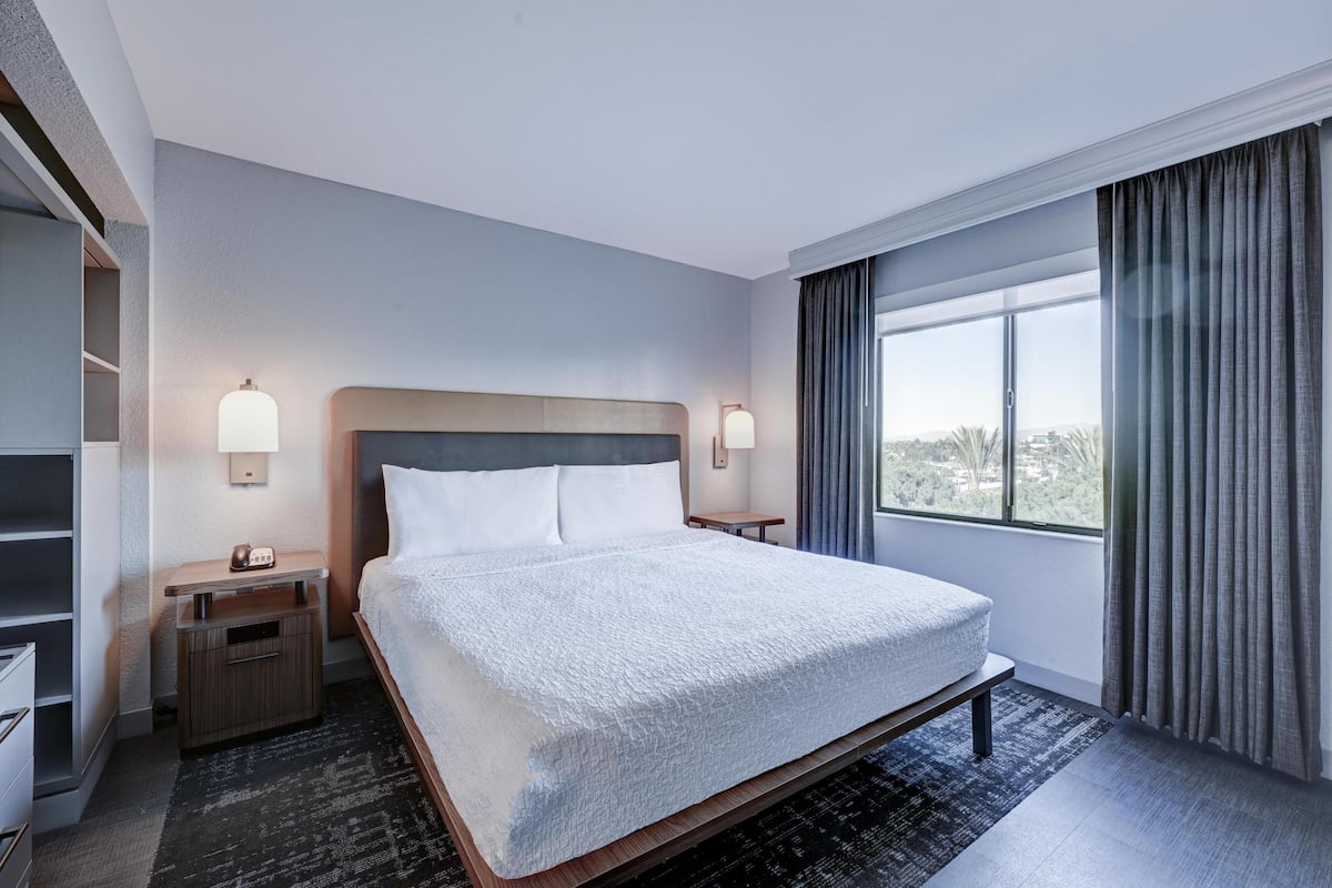 A hotel room with a large bed, bedside tables, a wardrobe, and a window with curtains.
