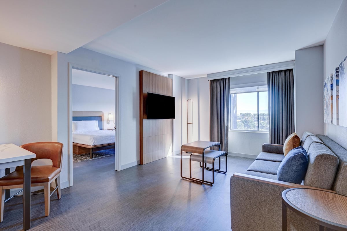 A hotel room with a bed, a TV, a sofa, a table, and a chair.