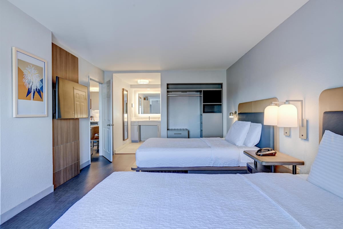A hotel room with two beds, a walk-in closet, a bathroom, and a hallway leading to other rooms.