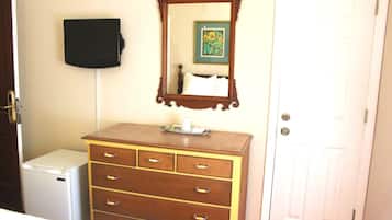 A room with a wooden dresser, a small white refrigerator, a mirror, and a door.