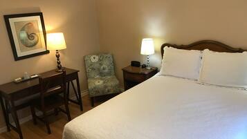 Une chambre d’hôtel comprenant un lit, un bureau, une chaise, deux tables de chevet avec des lampes et un tableau encadré au mur.
