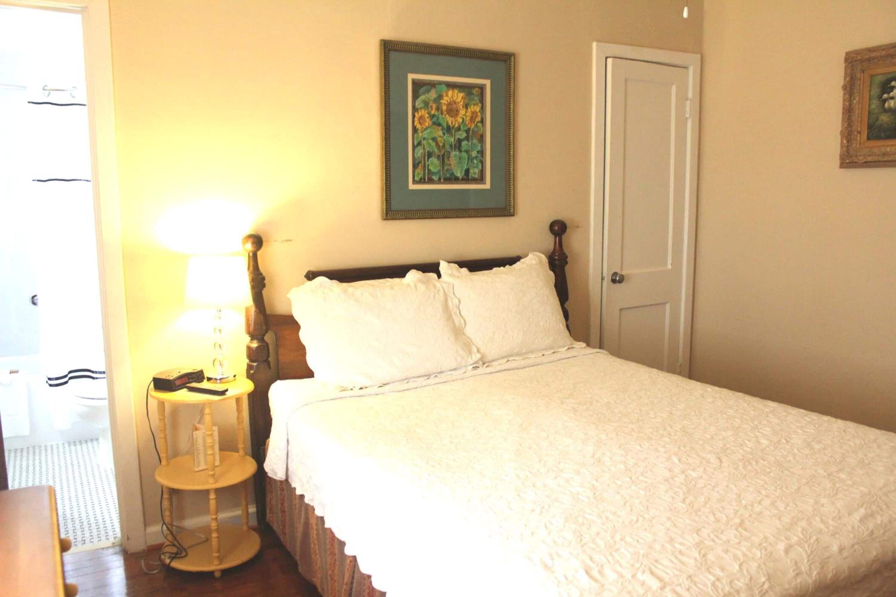 A neatly made bed with white linens, a bedside lamp, and a framed picture on the wall.