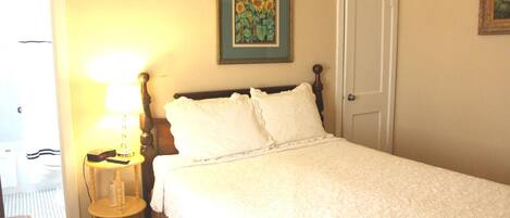 A neatly made bed with white linens, a bedside lamp, and a framed picture on the wall.