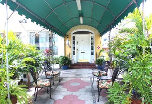 A covered patio area with outdoor seating, potted plants, and a building entrance. - The Inn on Third (St. Petersburg)