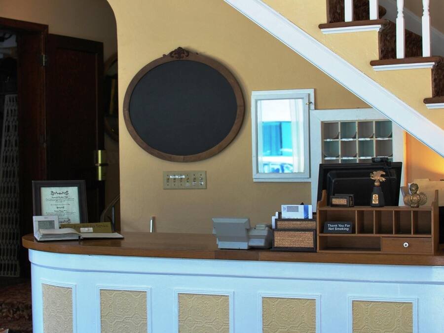 Un mostrador de recepción con un espejo redondo, un certificado enmarcado y una pequeña estatua. Una escalera con balaustres blancos conduce a un piso superior.
