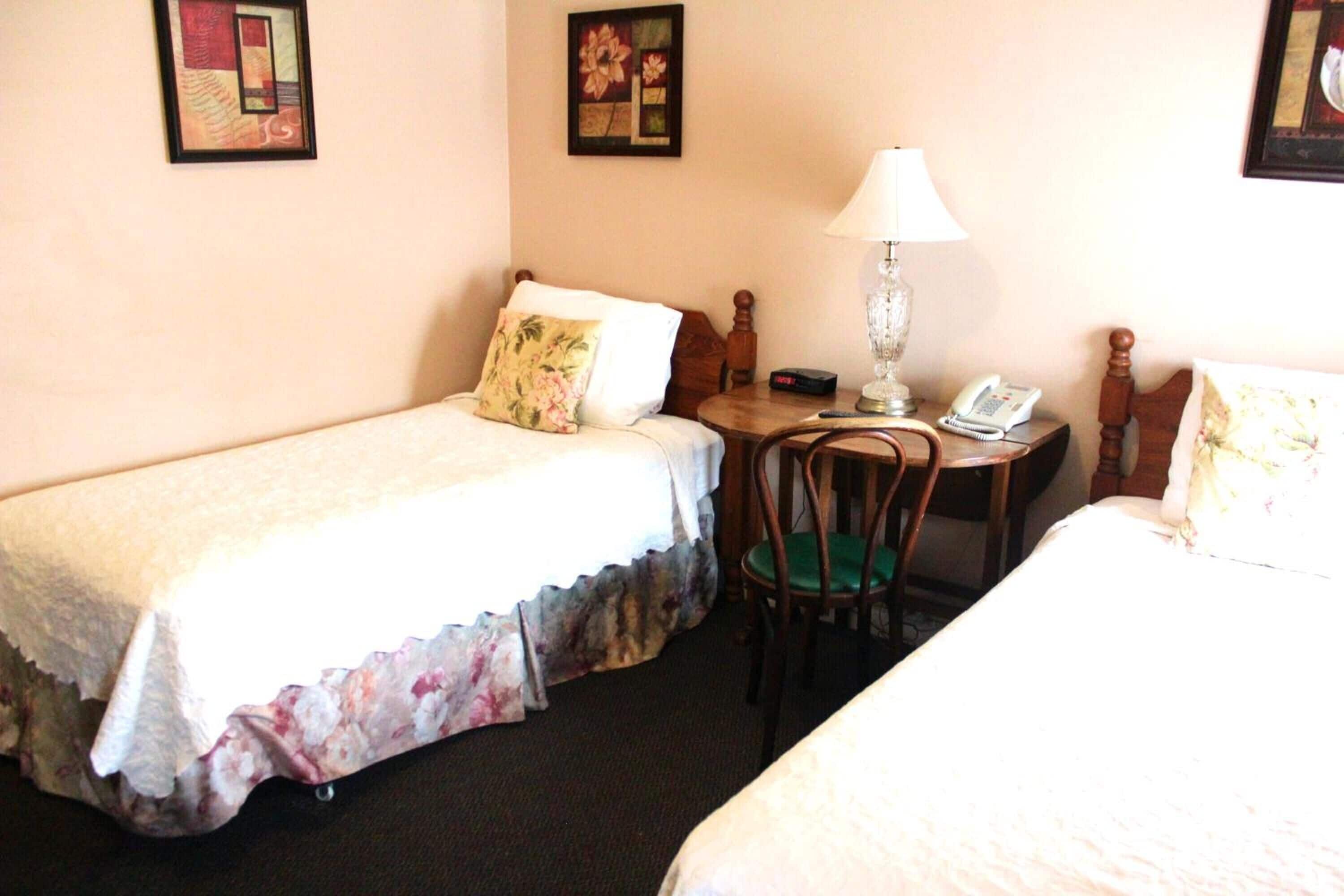 Ein Hotelzimmer mit zwei Einzelbetten, einem kleinen Tisch mit Lampe, einem Sessel und einem Telefon.