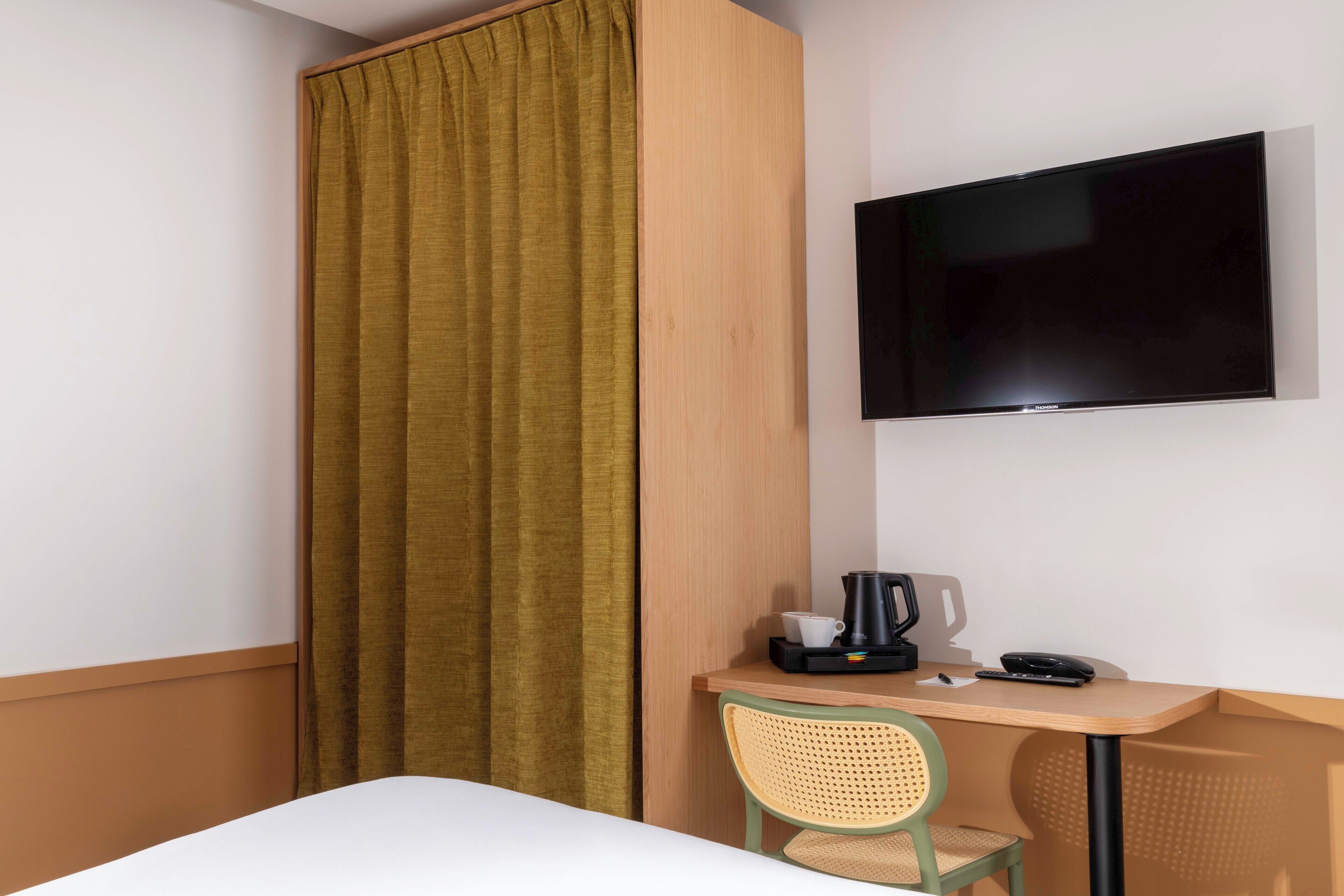 A hotel room with a bed, a desk with a chair, a television, and a curtain.