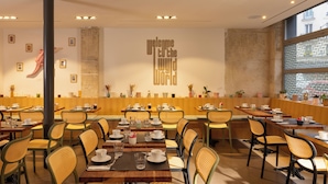 Un restaurante moderno con mesas de madera y sillas tejidas, un pilar grande y un letrero en la pared que dice 'Welcome to the World'.