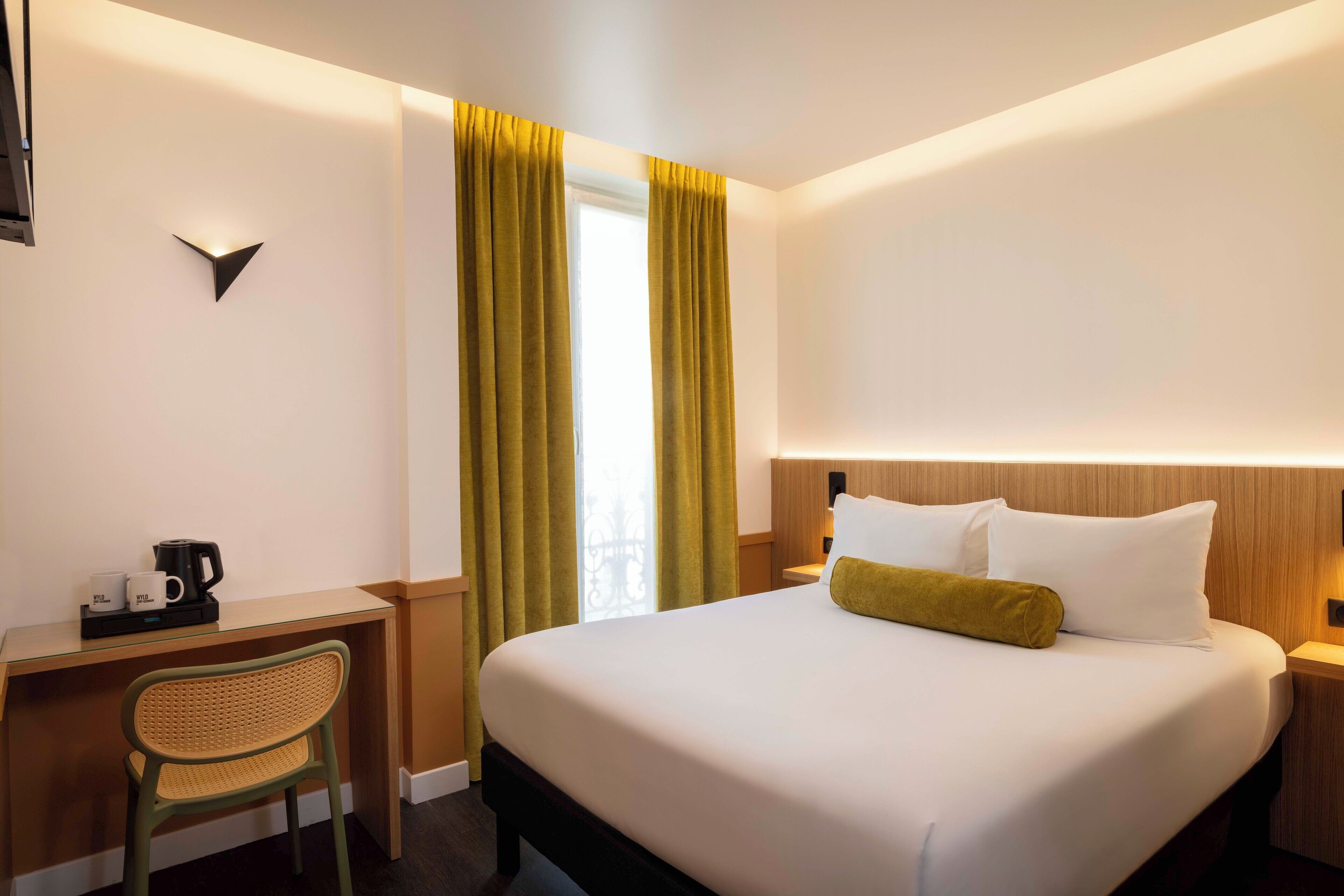 A hotel room with a bed, a desk with a chair, a coffee maker, and curtains.