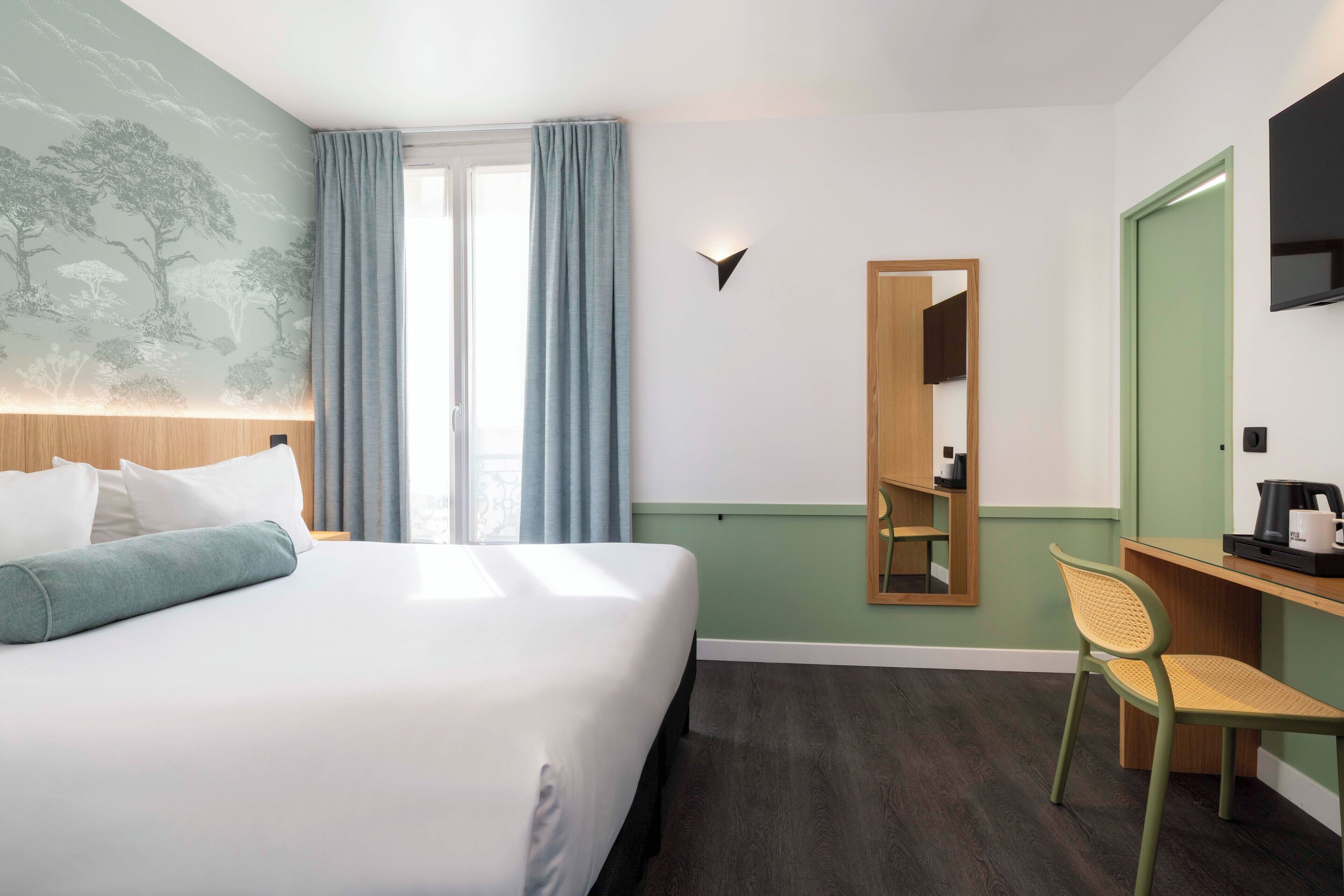 Una camera d'albergo con un letto, una scrivania, una sedia, uno specchio e una TV a muro.
