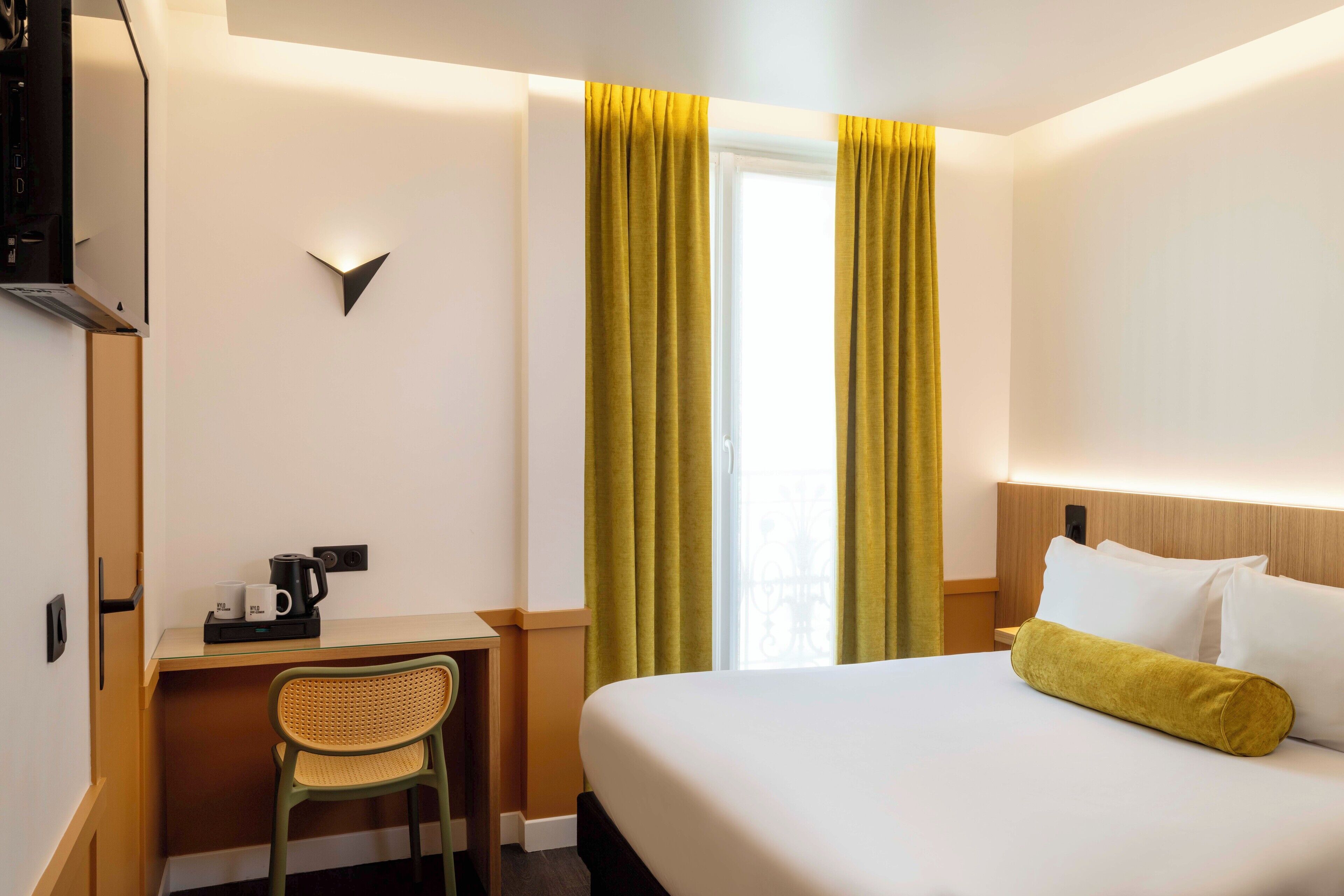 A hotel room with a bed, a desk with a chair, a coffee maker, and curtains.