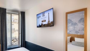 Habitación de hotel con cama, televisor de pared mostrando un código QR y ventana con cortinas.