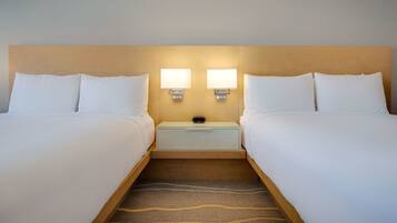 Quarto de hotel com duas camas, uma mesa de cabeceira com duas luminárias fixadas na parede e uma gaveta pequena.