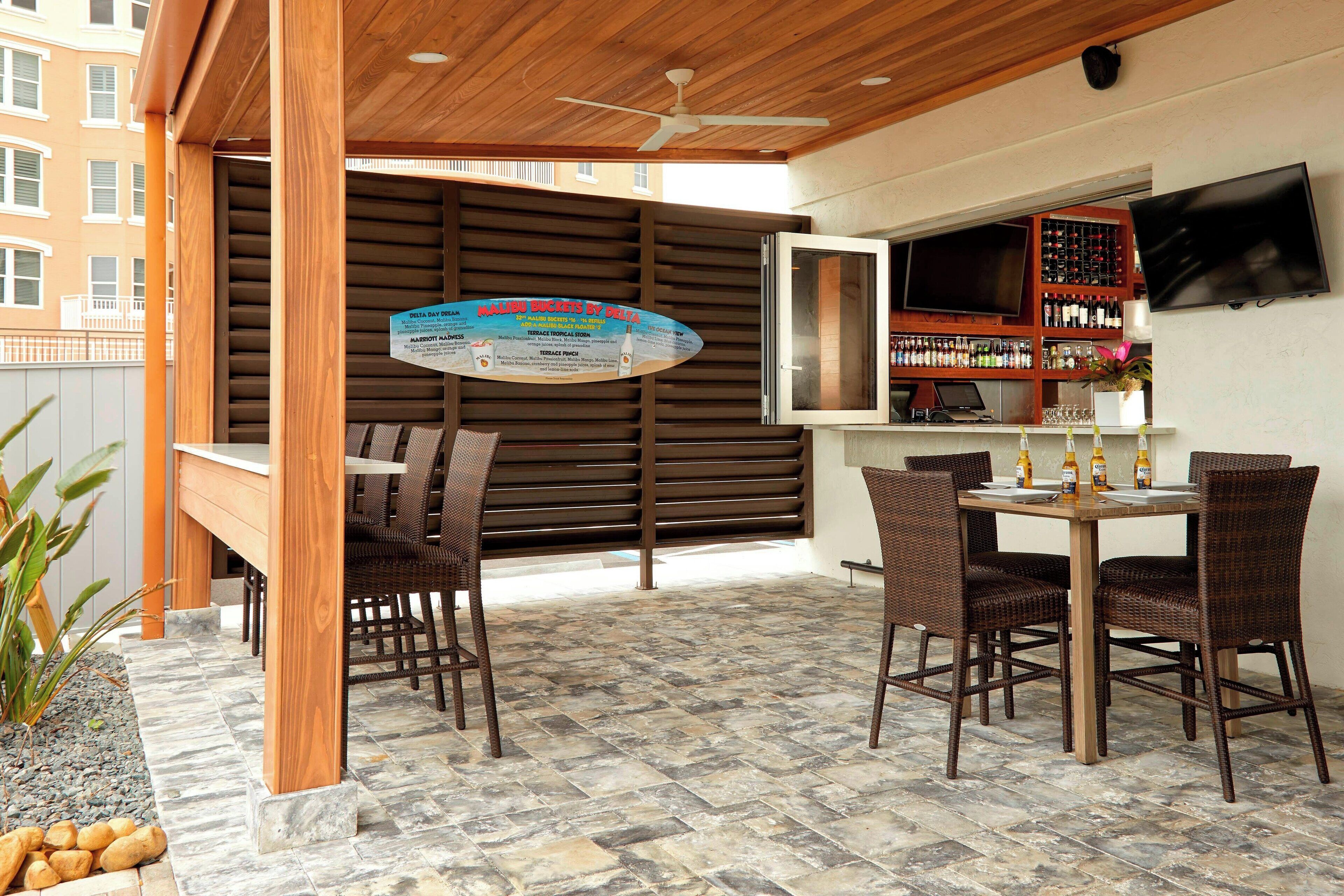 Un espace extérieur abrité, doté d’un plafond en bois, d’une table avec des chaises, d’un bar avec un téléviseur et d’un panneau indicateur.