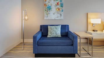 A blue sofa with a patterned pillow, a floor lamp, a small table, and a wall-mounted lamp.