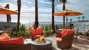 A patio area with wicker furniture, orange cushions, and a fire pit.