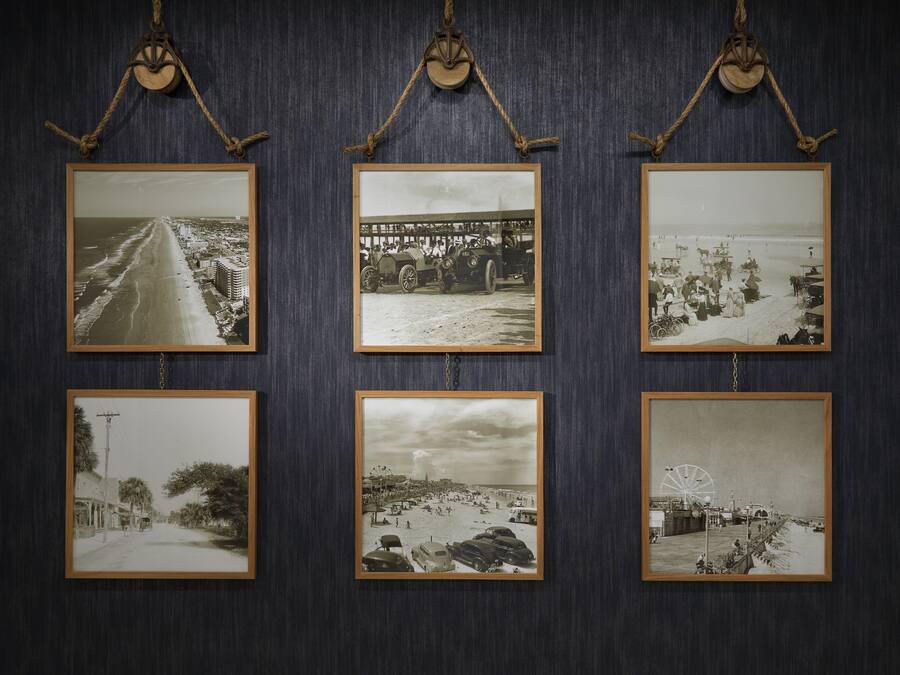 Six black and white photographs of beach scenes, each framed and hung on a dark wall.