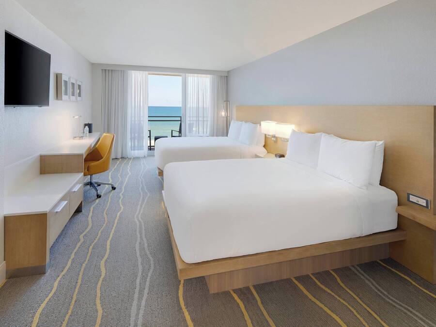 A hotel room with a large bed, a desk, a chair, a TV, and a view of the ocean.