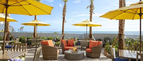 An outdoor patio with yellow umbrellas, wicker furniture, and a fire pit.