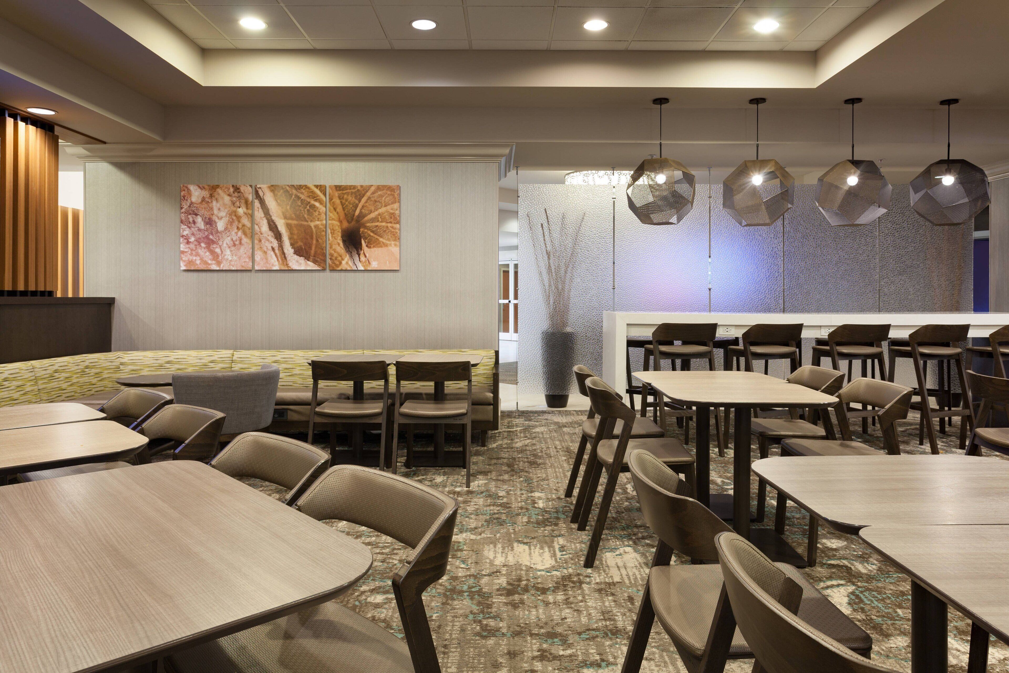 Une salle à manger d’hôtel avec plusieurs tables et chaises, un comptoir de réception et un grand tableau abstrait accroché au mur.