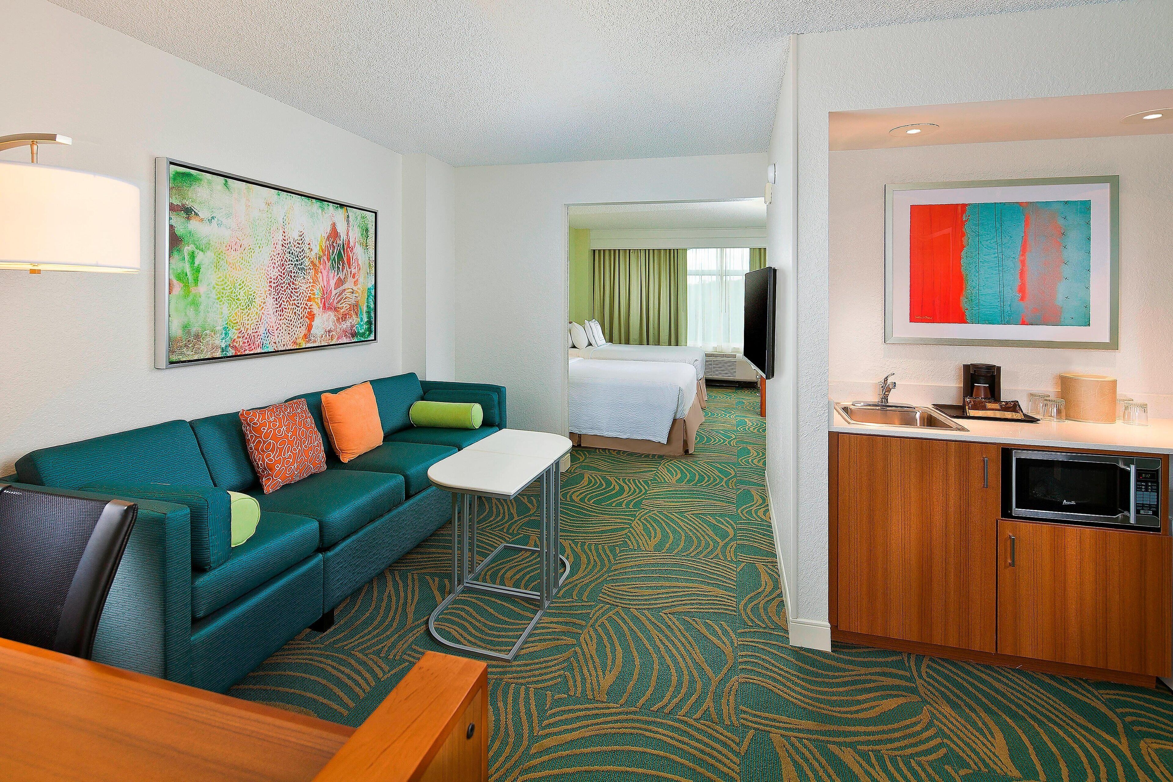A hotel room with a sofa, a small table, a bed, a TV, a microwave, and a sink.