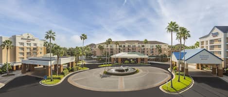 A hotel complex with multiple buildings, a central courtyard with a fountain, and palm trees.