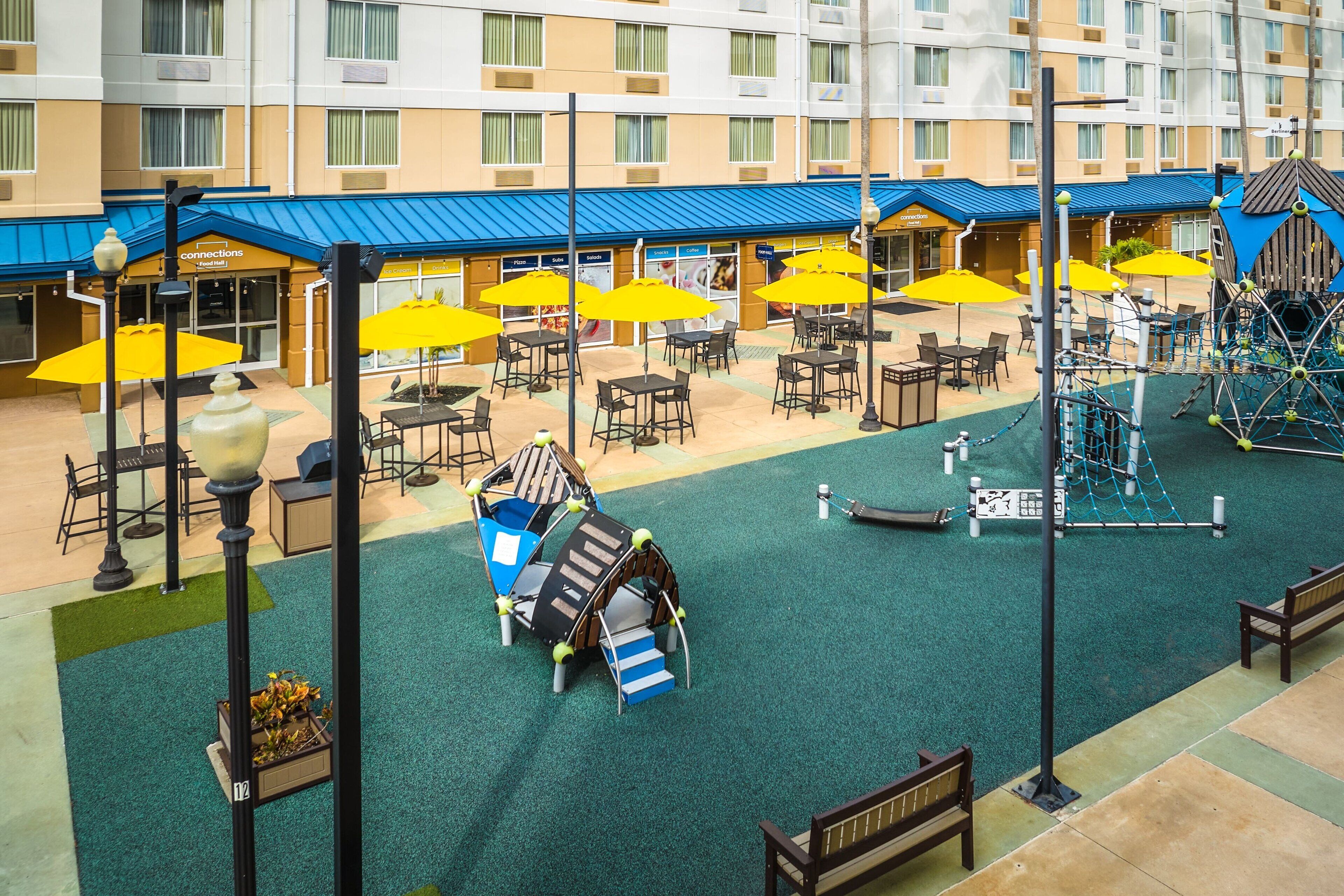 Un'area patio esterna con ombrelloni gialli, posti a sedere all'aperto e un'area giochi.