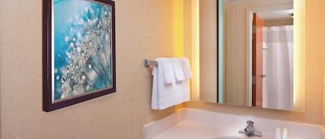 A bathroom with a white sink, a framed artwork, and a mirror reflecting a shower area.