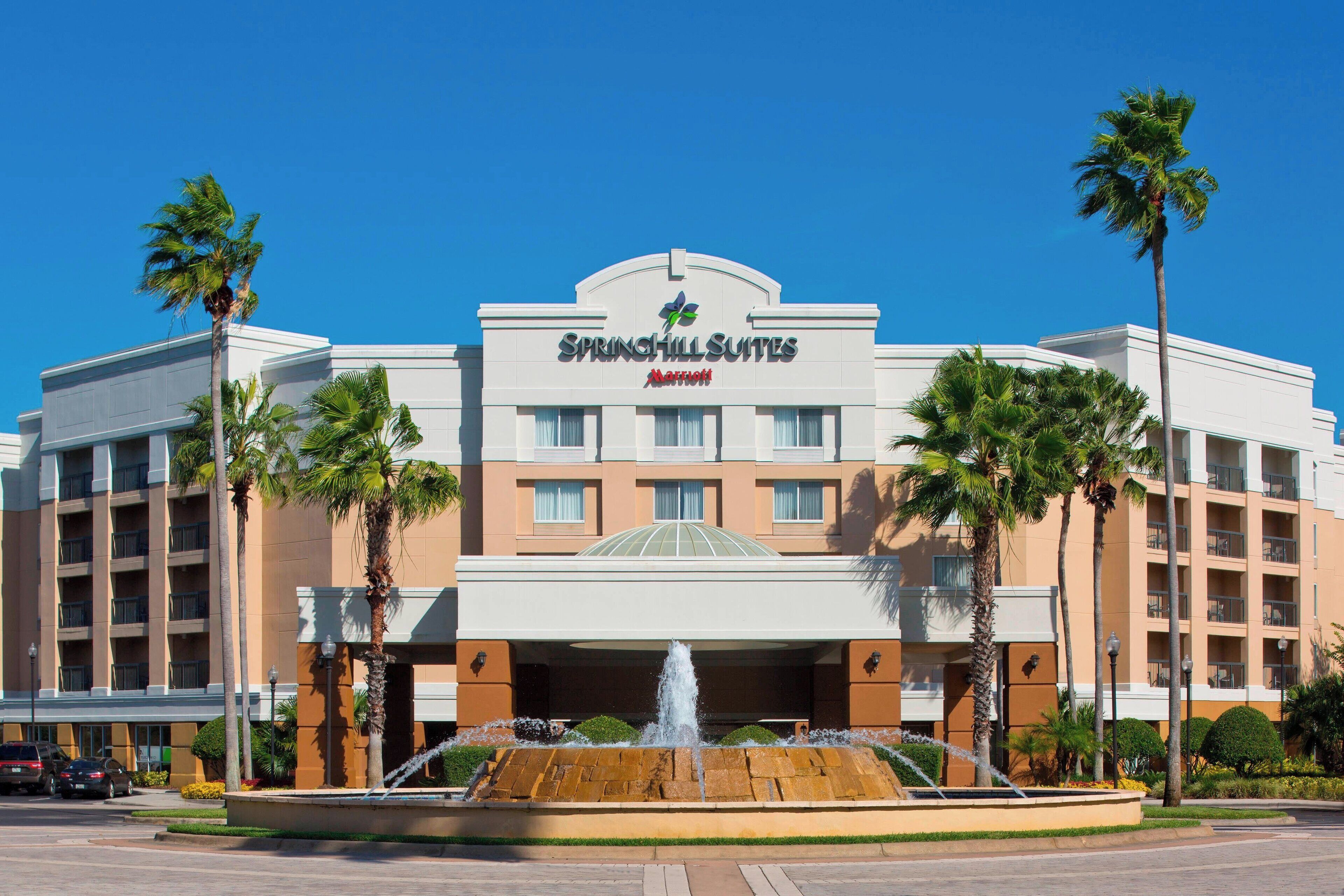 A hotel with a fountain in front, palm trees, and a clear blue sky.
