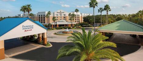 A hotel with a blue roof, a central fountain, and palm trees.