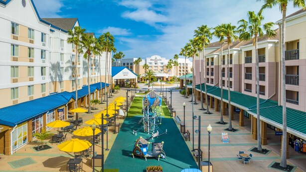 Cortile di un hotel con posti a sedere all'aperto, palme e area giochi per bambini.