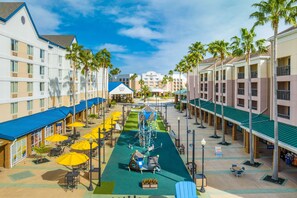 Un patio de hotel con mobiliario exterior, palmeras y una zona de juegos para niños.