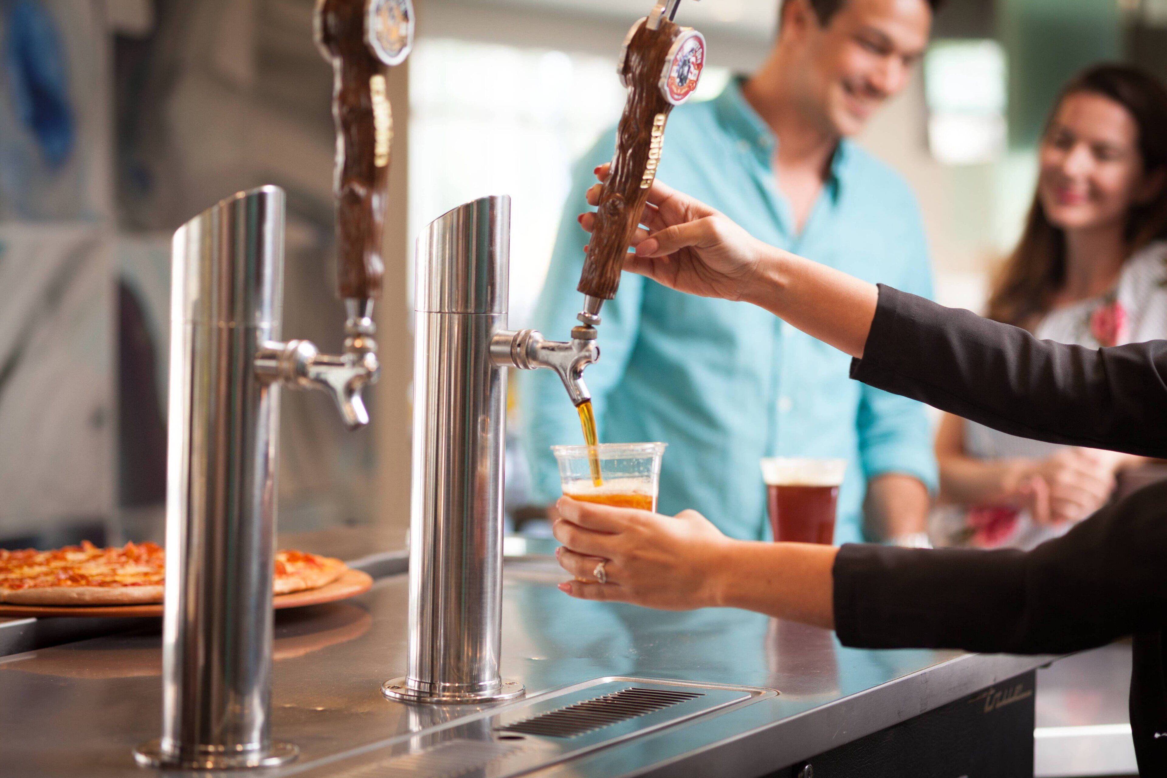 A bar area with stainless steel taps and a person pouring a drink into a cup.