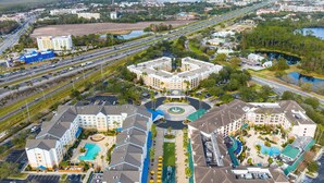 Un hotel con un cortile centrale, diverse piscine e un'ampia area di parcheggio.