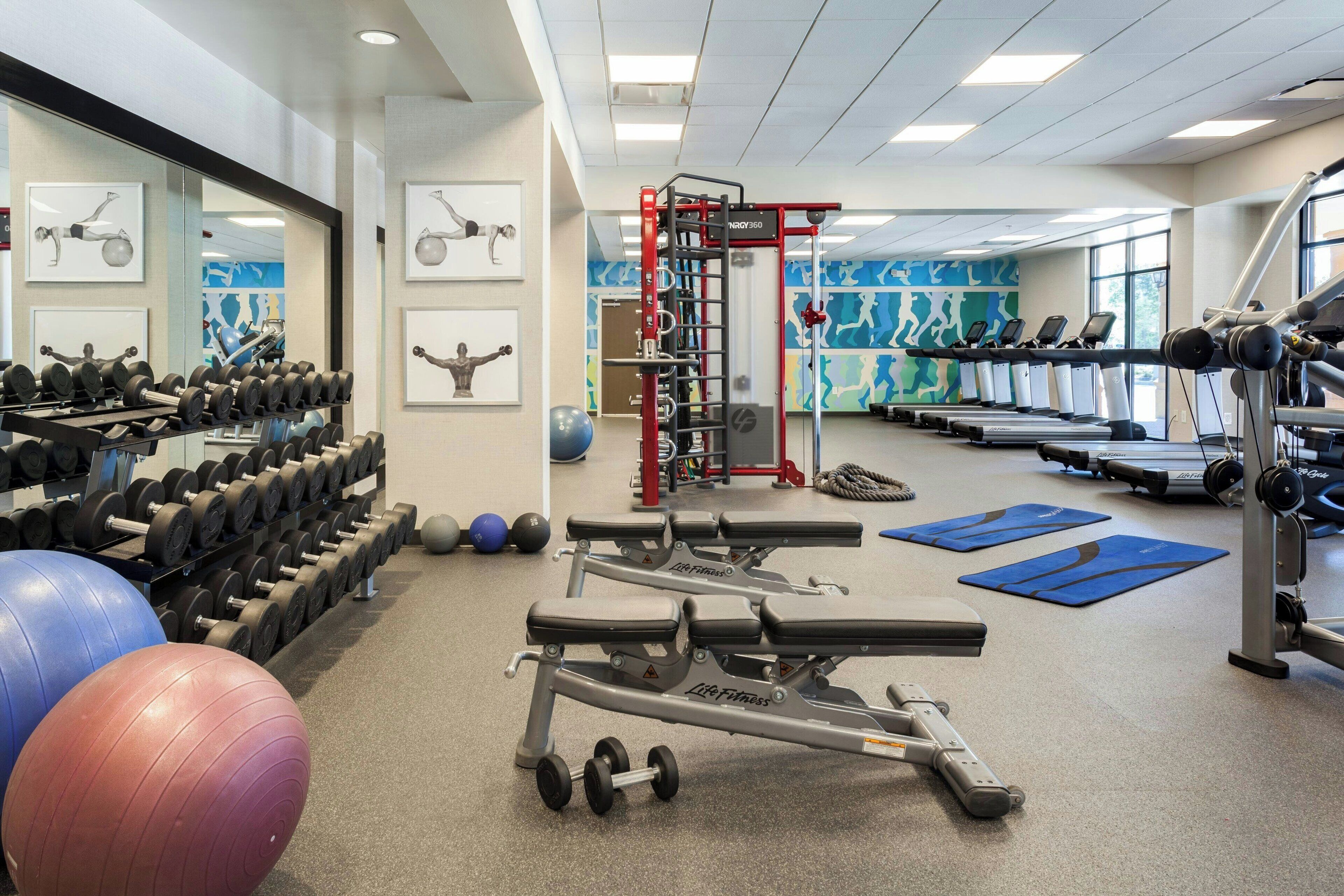 Une salle de sport équipée d’haltères, de ballons d’exercice, de tapis de course et d’un banc de musculation.
